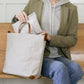 A woman is shown sitting, placing a washable paper pouch into a grey washable paper tote bag.