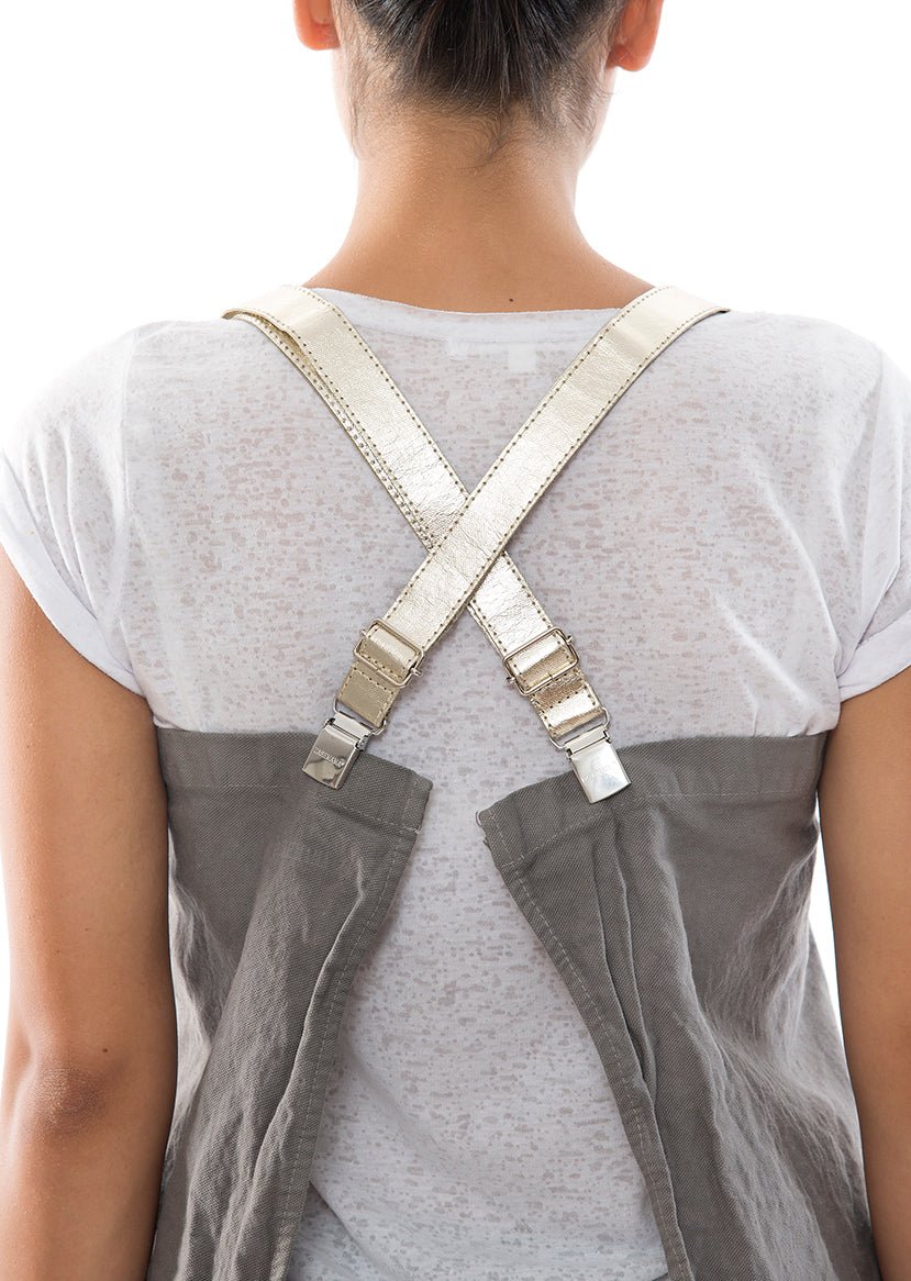 The back of a person is shown. They are wearing a dark grey cotton apron which fastens with silver washable paper braces crossed over the back of the person's shoulders.