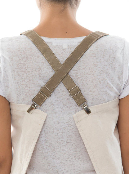 The back of a person is shown. They are wearing a white cotton apron which fastens with olive washable paper braces crossed over the back of the person's shoulders.