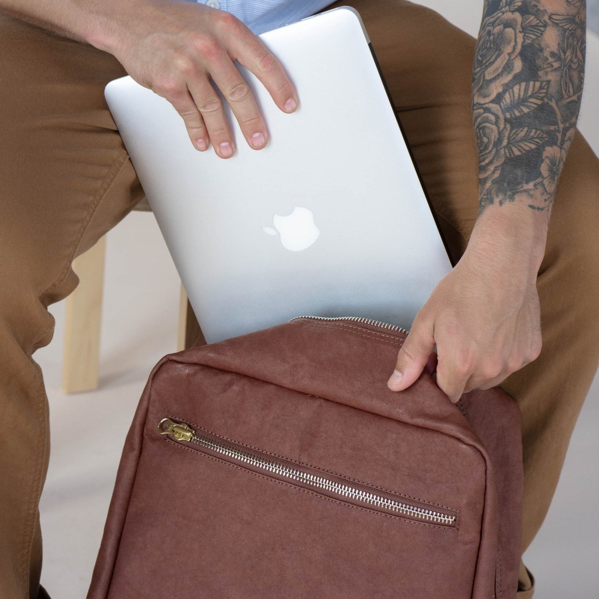 A man is shown sliding a laptop into a square washable paper backpack.