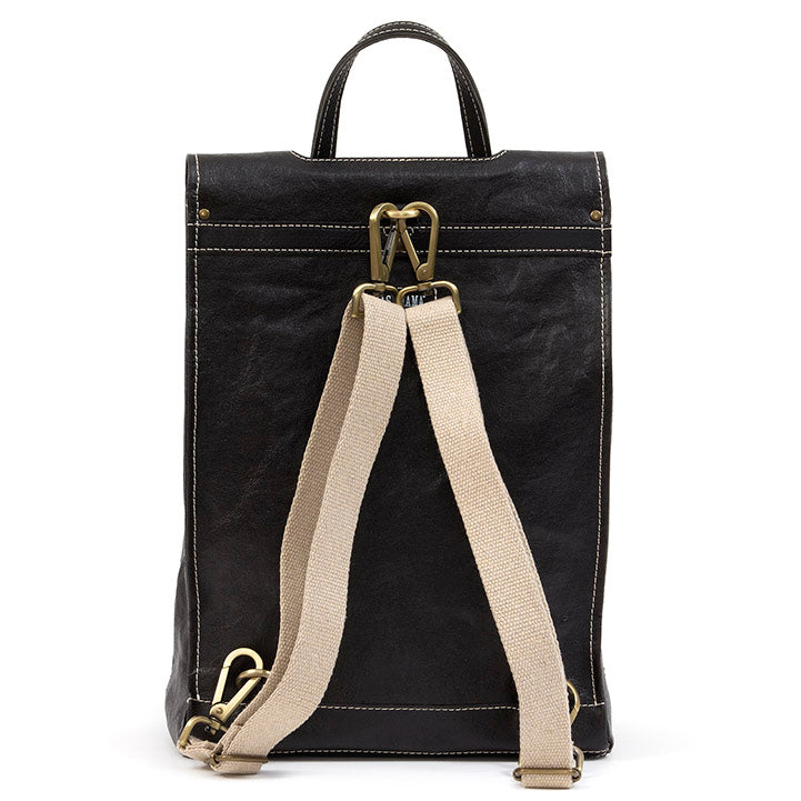A black washable paper backpack is shown from the back angle. It features white stitching, a top handle and cream cotton canvas straps with gold metallic hardware. 