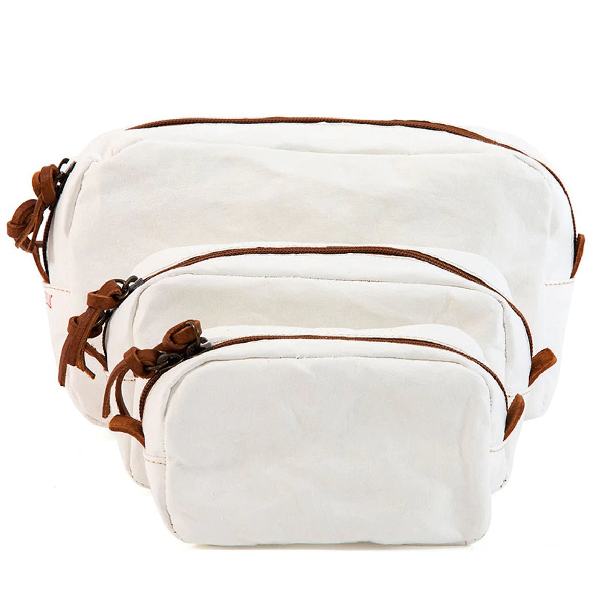 A set of three washable paper toiletry bags is shown. Each bag has a brown zip with a tan leather zip pull. The smallest bag is at the front, then the medium bag and the large size at the back. The bags shown are white in colour.