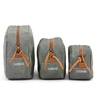 The image is of three washable paper toiletry bags, the largest is on the right, then the medium size and then the smallest size. The bags are closed and the image shows the UASHMAMA logo on the end of each bag. The bags shown are dark grey in colour.