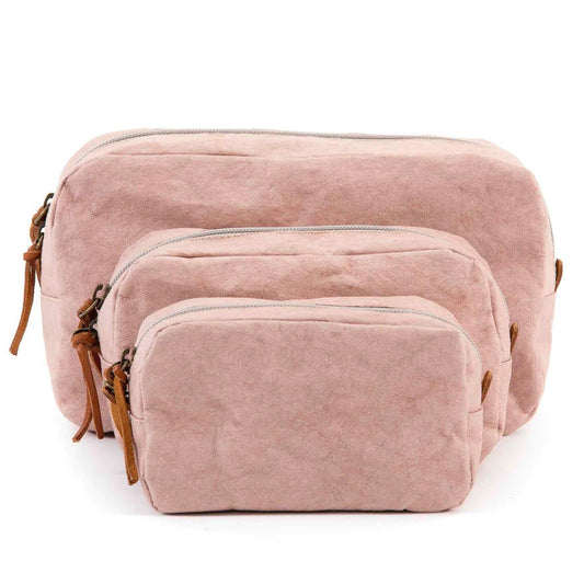 A set of three washable paper toiletry bags is shown. Each bag has a brown zip with a tan leather zip pull. The smallest bag is at the front, then the medium bag and the large size at the back. The bags shown are pale pink in colour.