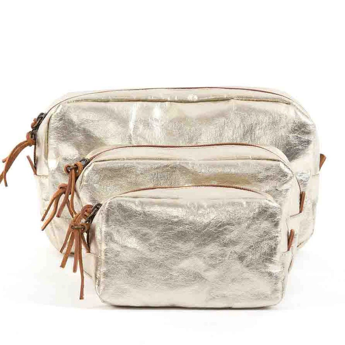A set of three washable paper toiletry bags is shown. Each bag has a brown zip with a tan leather zip pull. The smallest bag is at the front, then the medium bag and the large size at the back. The bags shown are platinum metallic in colour.