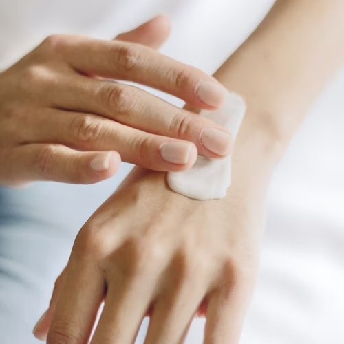 A woman is shown rubbing body milk into the back of her left hand.