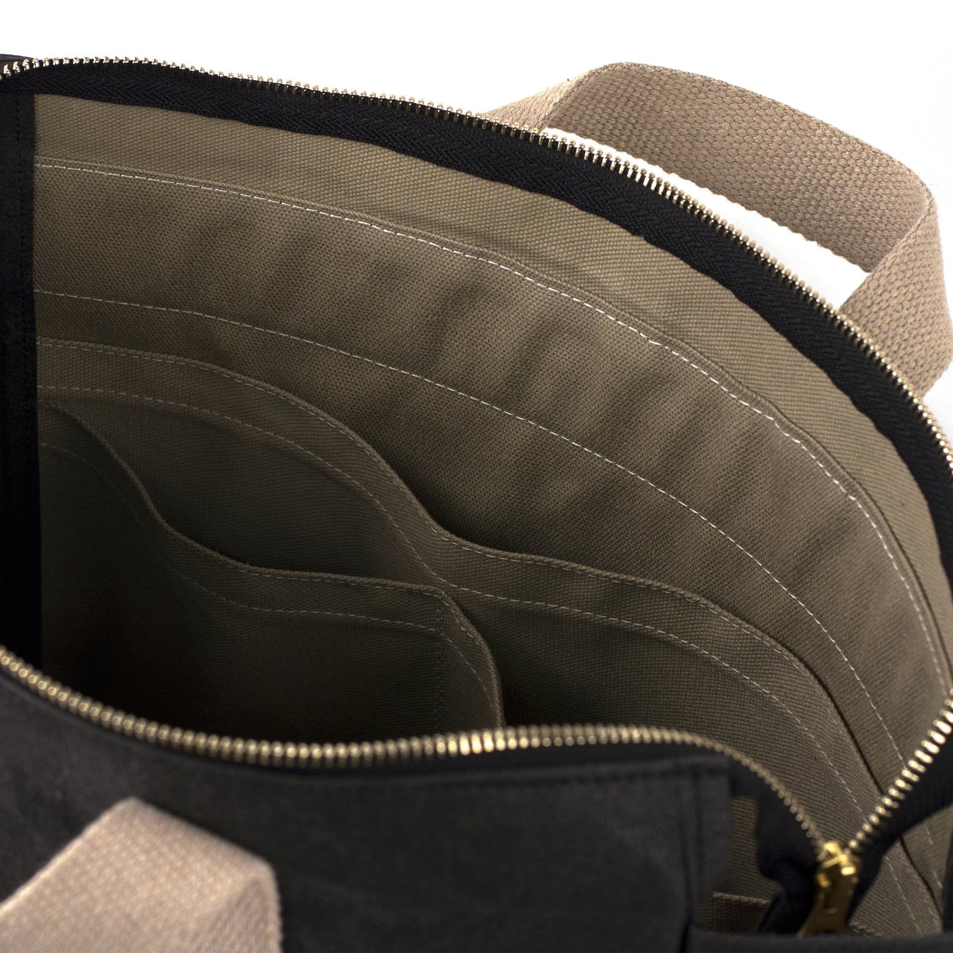 A black washable paper backpack is shown close up from a top-down angle. It features a khaki lining, with inside pockets and white stitching. It has a gold zip and two natural toned canvas handles.