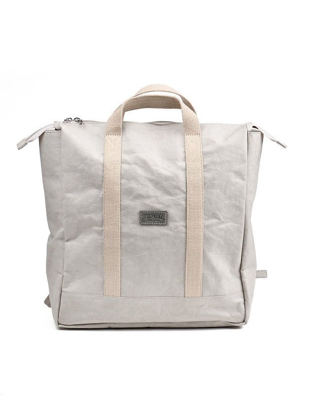 A white washable paper backpack is shown from the front. Square in design, it features a top zip and two cream canvas handles at the front and at the back.