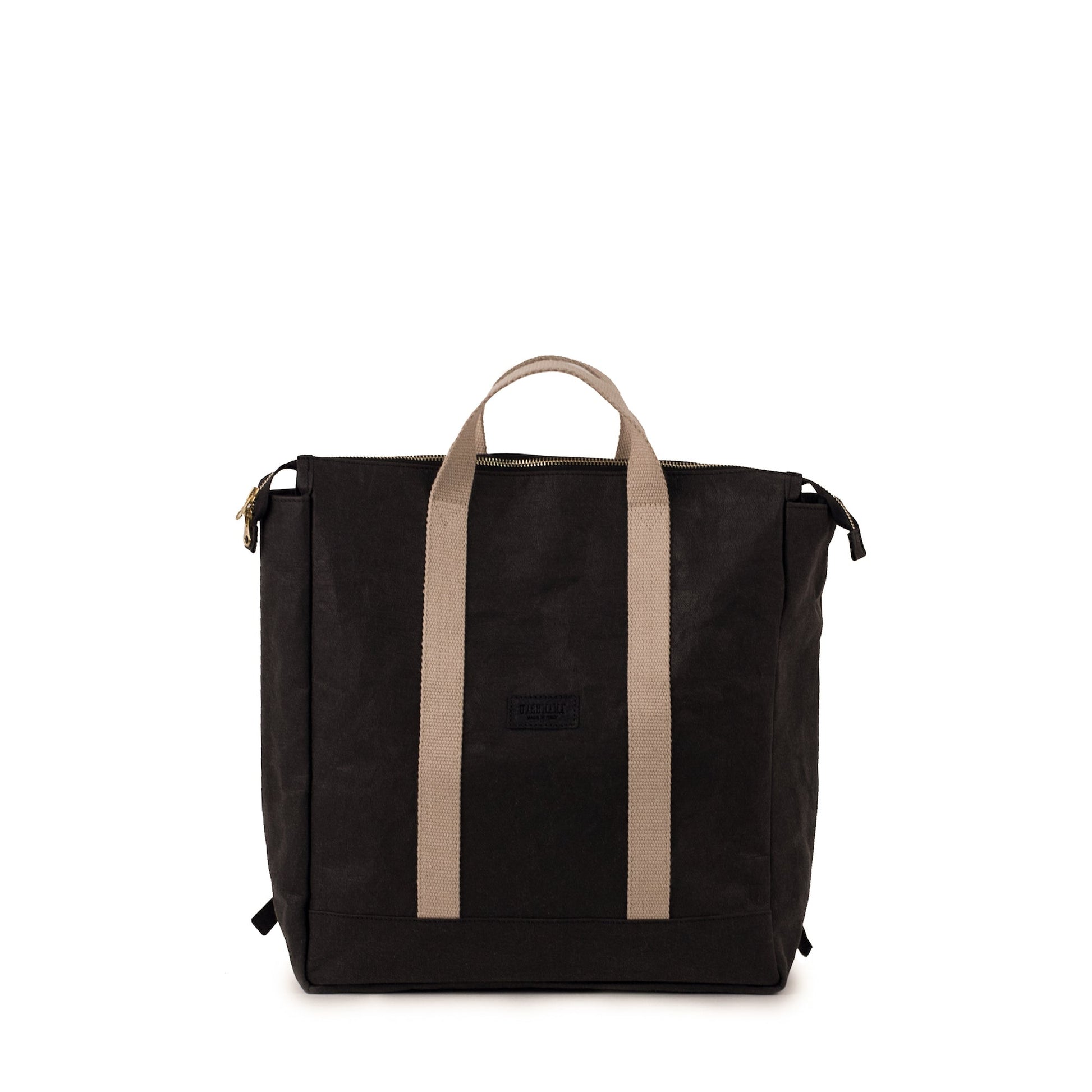 A black washable paper backpack is shown from the front. Square in design, it features a top zip and two cream canvas handles at the front and at the back.