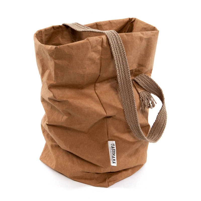 A tan coloured washable paper bag with a single cotton carry strap in brown. The top is displayed open and rolled down, with a natural toned UASHMAMA logo tab on the right hand side.