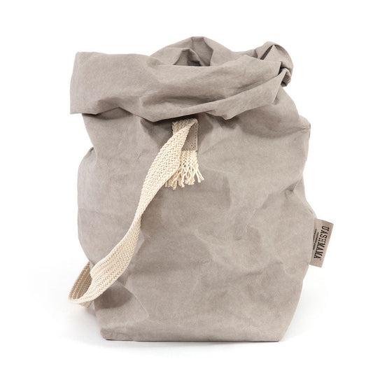 A grey washable paper bag with a single cotton carry strap in cream. The top is displayed open and rolled down, with a natural toned UASHMAMA logo tab on the right hand side.