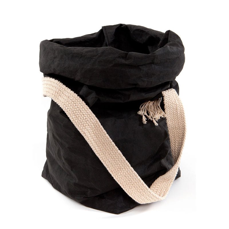 A black washable paper bag with a single cotton carry strap in cream. The top is displayed open and rolled down, with a natural toned UASHMAMA logo tab on the right hand side.