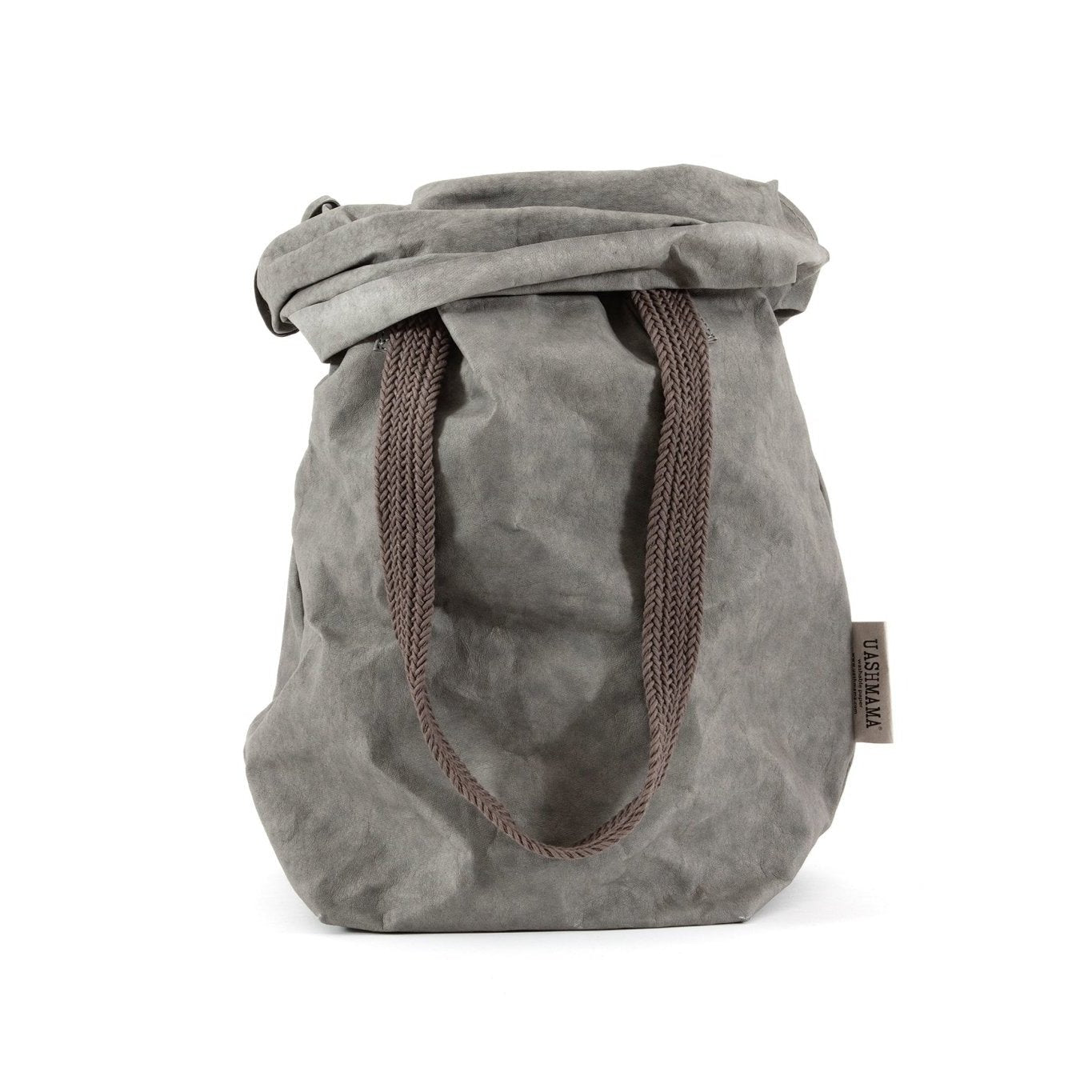 A mid grey washable paper bag is shown from the front with the top rolled down. It features two brown cotton straps (one visible in this image) and a natural toned UASHMAMA logo tab at the left hand side.