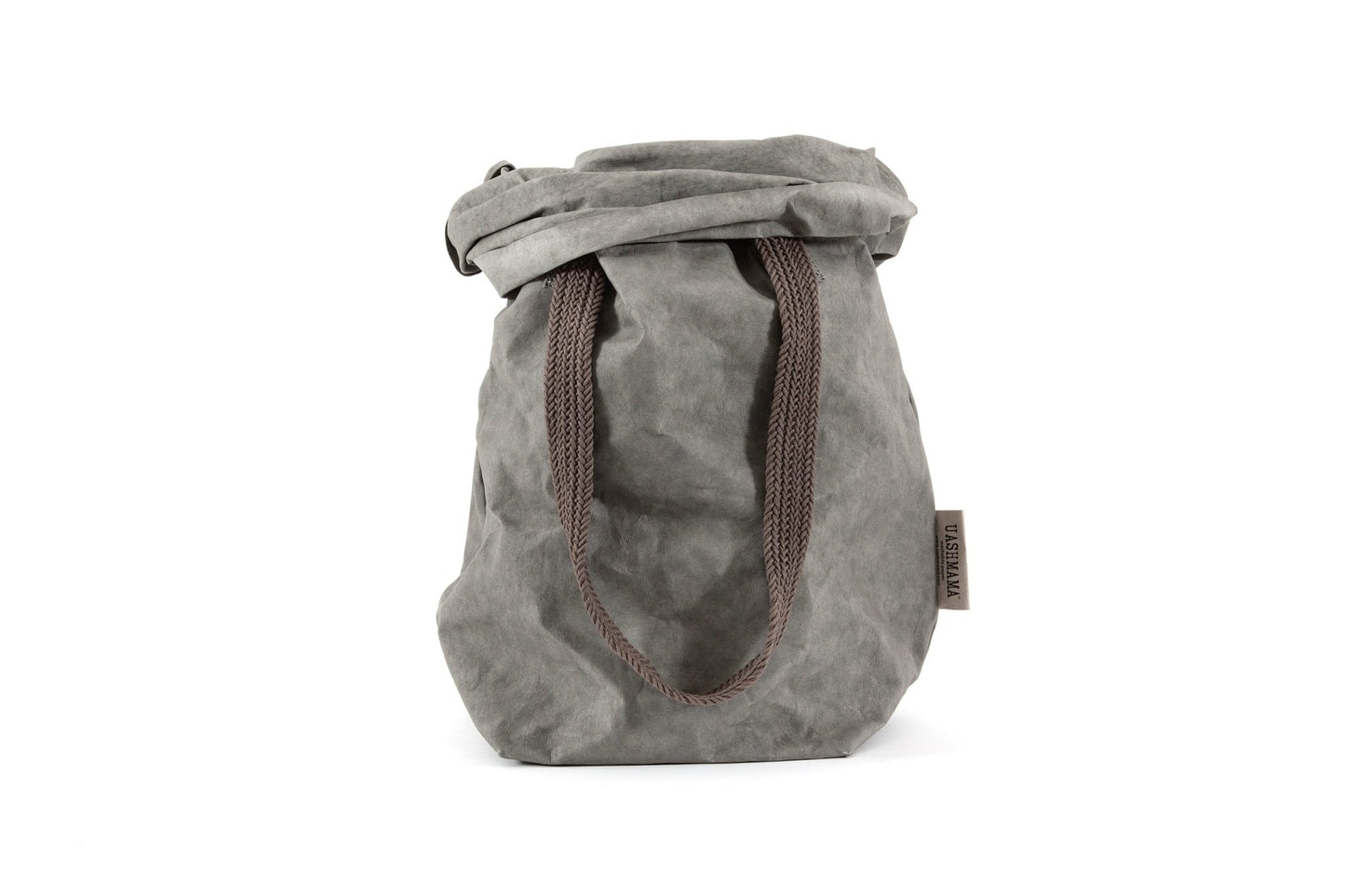A mid grey washable paper bag is shown from the front with the top rolled down. It features two brown cotton straps (one visible in this image) and a natural toned UASHMAMA logo tab at the left hand side.