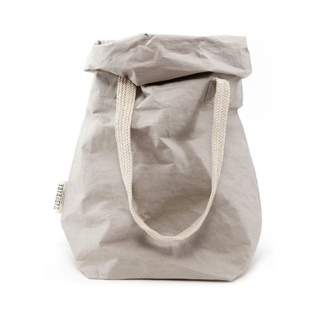 A dove grey washable paper bag is shown from the front with the top rolled down. It features two cream cotton straps (one visible in this image) and a natural toned UASHMAMA logo tab at the left hand side.