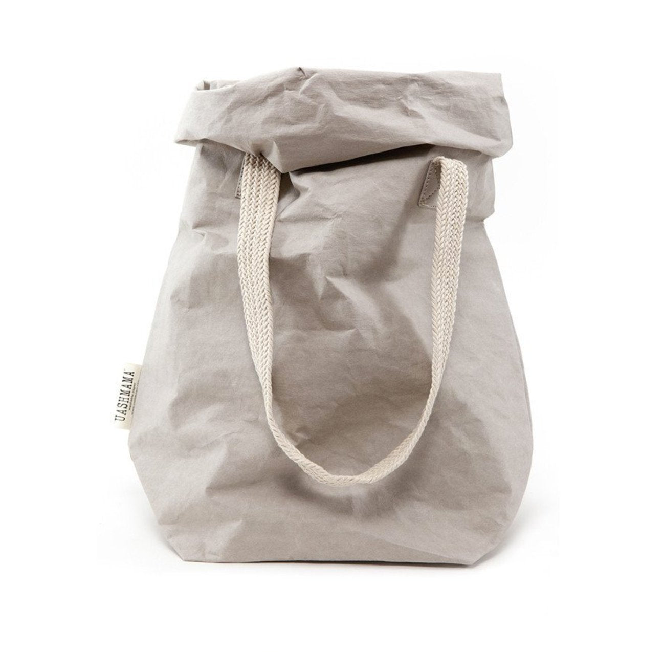 A dove grey washable paper bag is shown from the front with the top rolled down. It features two cream cotton straps (one visible in this image) and a natural toned UASHMAMA logo tab at the left hand side.