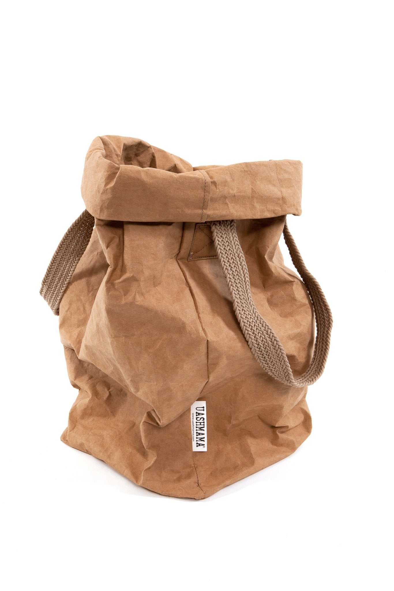 A natural tan coloured washable paper bag is shown from a 3/4 angle with the top rolled down. It features two brown cotton handles and a natural toned UASHMAMA logo tab at the left hand side.