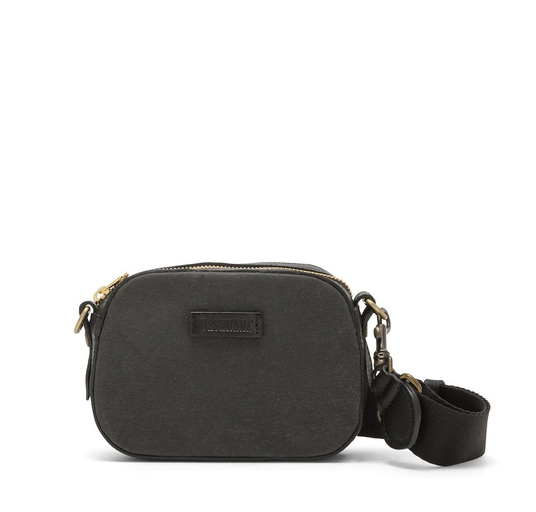 A small washable paper cross-body bag is shown with a front tab bearing the UASHMAMA logo in a small font. The bag is shown in black, with a darker black cotton strap with antique brass hardware.