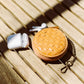 A tan woven washable paper round coin purse sits on wooden slats, with an antique brass attachment chain. A pair of Air Pods sit at left.