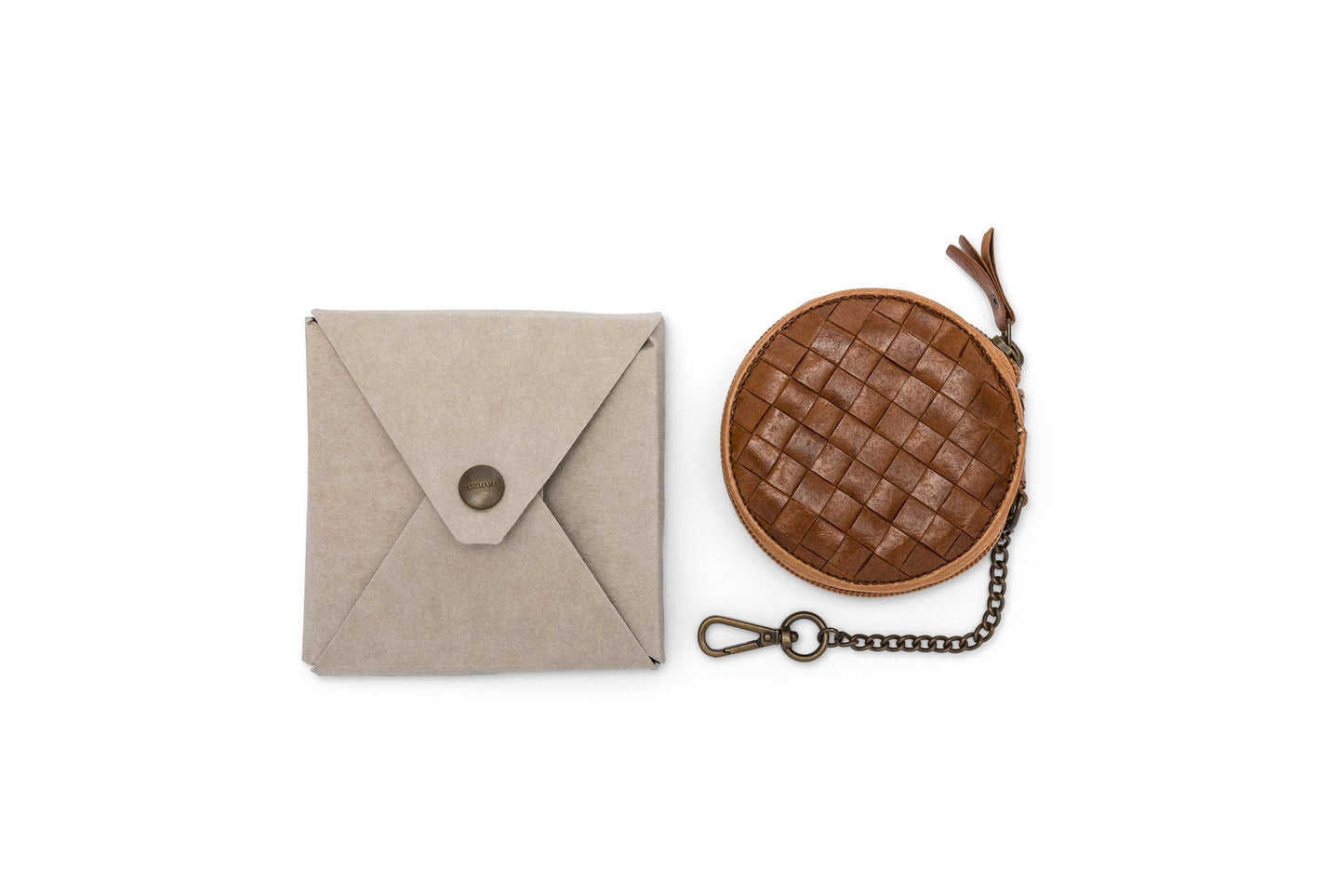 A brown woven washable paper round coin purse featuring a brown zip tab and an antique brass coloured attachment chain sits to the right of a square beige washable paper envelope of the same size.