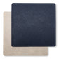 Two square washable paper placemats are shown one on top of the other. The one in the foreground is navy and the one at the rear is beige.