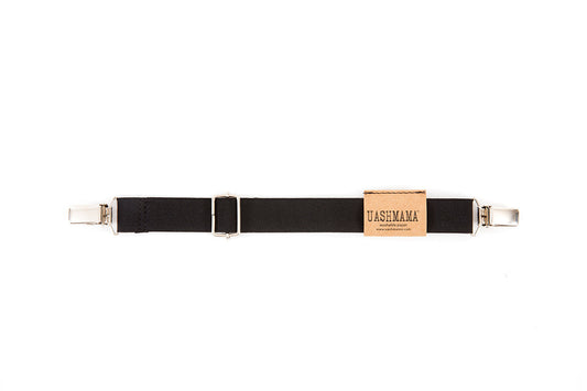 An apron strap is shown, with a metal clip at each end. It is black in colour, and features a brown UASHMAMA logo tab. 