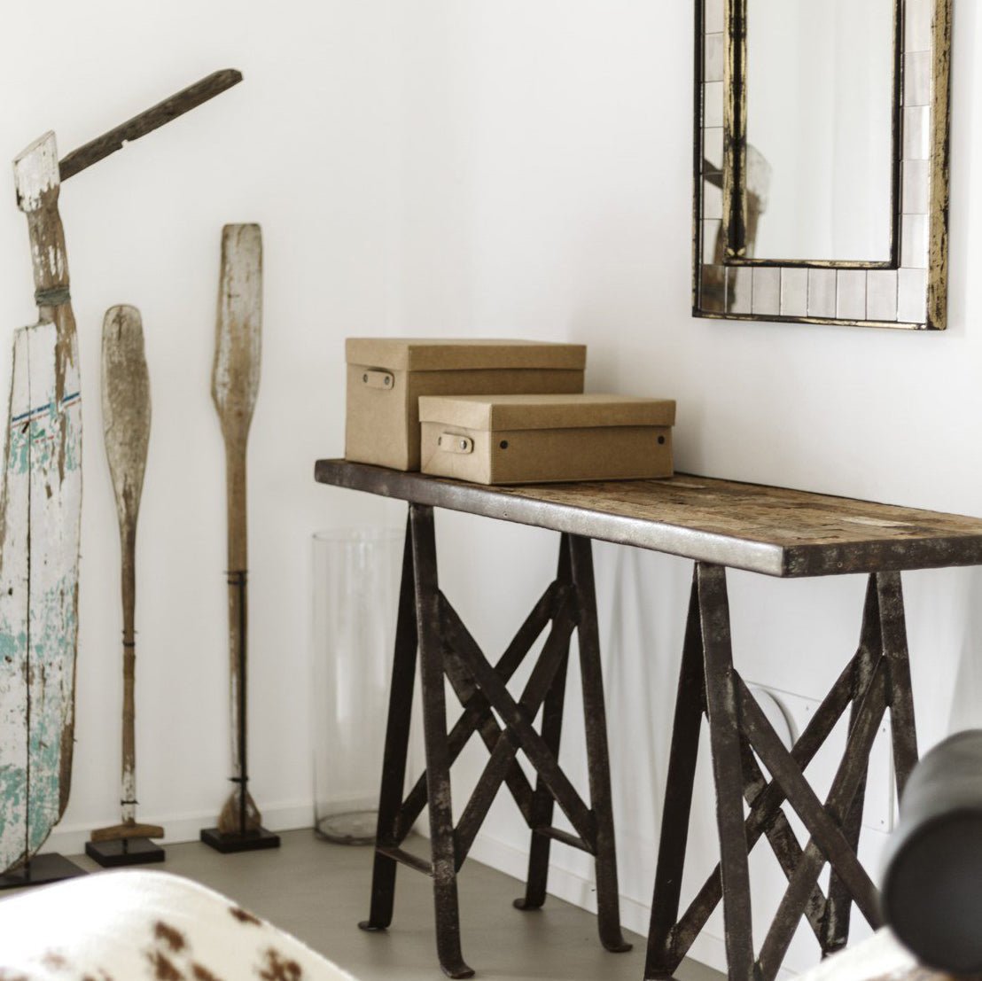 Two tan washable paper lidded boxes are shown on a metal and wood console table in a home setting, under a mirror.