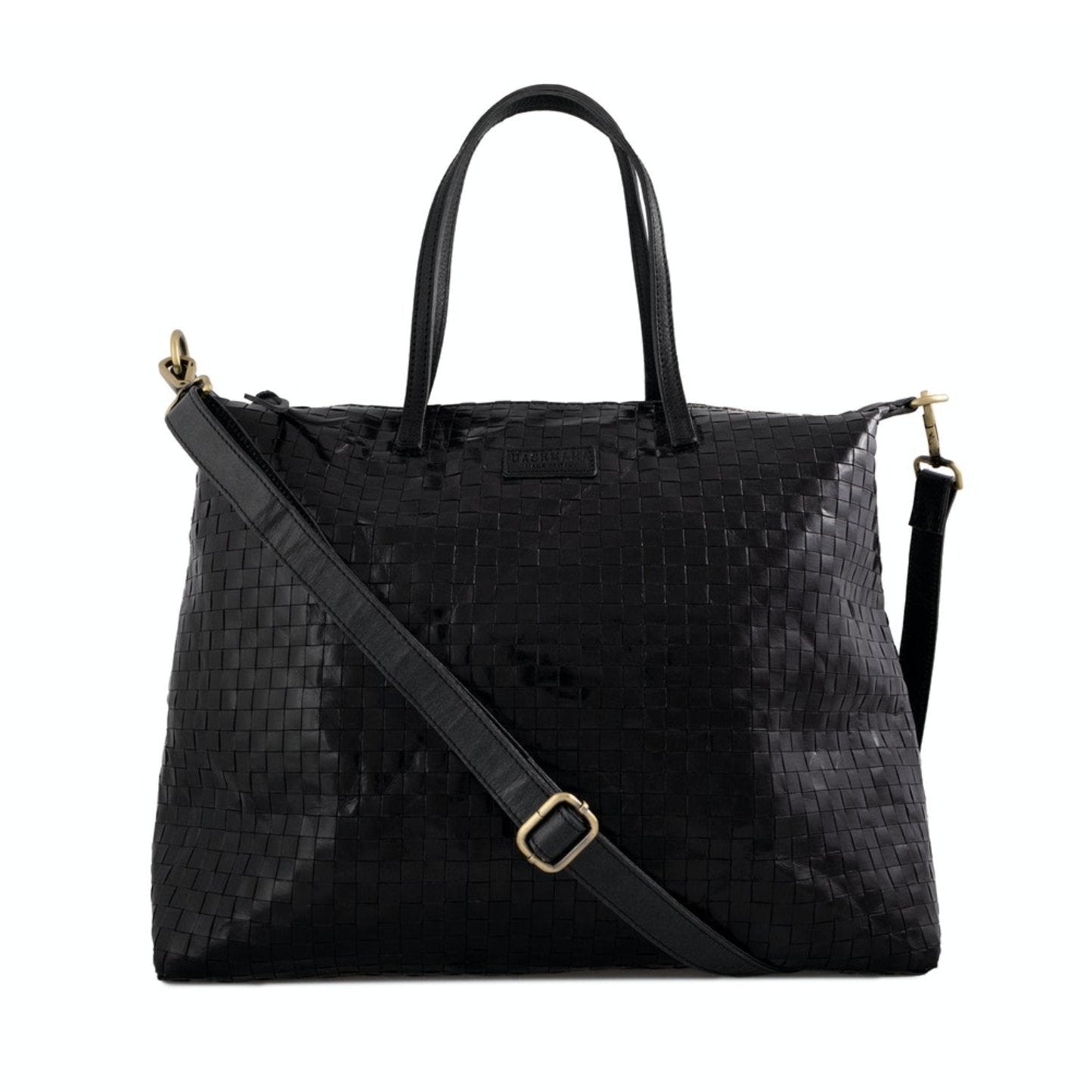 A large black woven washable paper tote is shown from the front angle. It features two top handles and a long washable paper black shoulder strap with brass hardware.