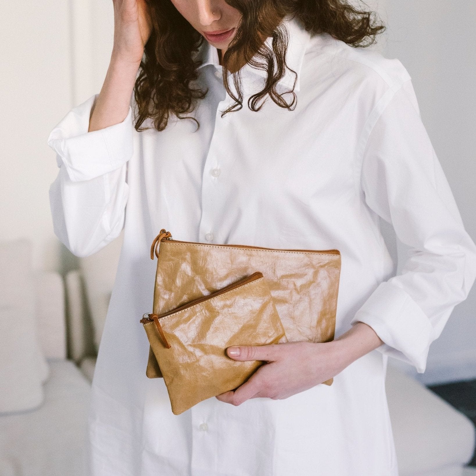 A woman wearing a white shirt is shown holding two washable paper pouches in varying sizes, both tan in colour.