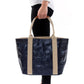 A woman in casual clothing is shown holding a navy metallic washable paper tote bag with two beige cotton canvas top handles.