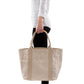 A woman in casual clothing is shown holding a cream washable paper tote bag with two beige cotton canvas top handles.