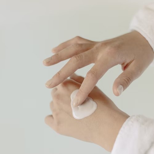 A woman is shown applying hand cream to the back of her hand.