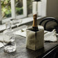 A grey washable paper cooler is shown holding a bottle of champagne on a table setting. It features a washable paper side tab closure with a metal stud.