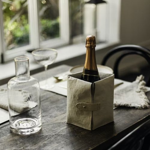A grey washable paper cooler is shown holding a bottle of champagne on a table setting. It features a washable paper side tab closure with a metal stud.