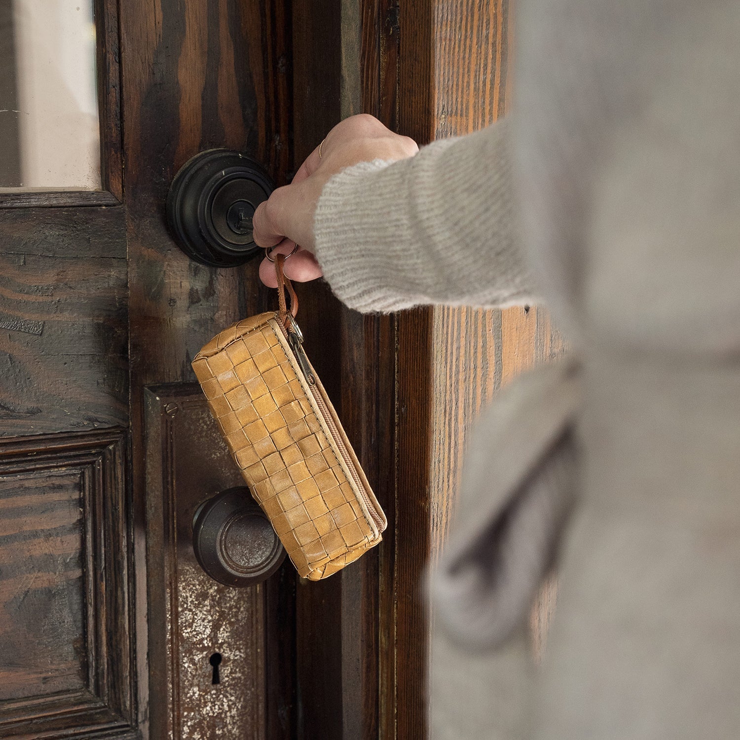 A person is shown unlocking a door with a key that is attached to a tan woven washable paper key holder.