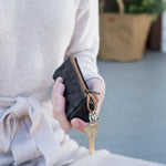 A woman is shown holding a black washable paper key holder with a gold key dangling from the inner attachment. A tan washable paper tote is shown in the background.