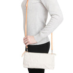 A woman is shown smiling in casual clothing, wearing a small washable paper handbag in white, with a tan long strap.