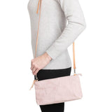 A woman is shown from the side in casual clothing, wearing a small washable paper handbag in dusky pink, with a tan long strap.