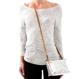 A woman is shown in casual clothing wearing a metallic silver washable paper small handbag in a cross-body style, by way of a long tan strap.