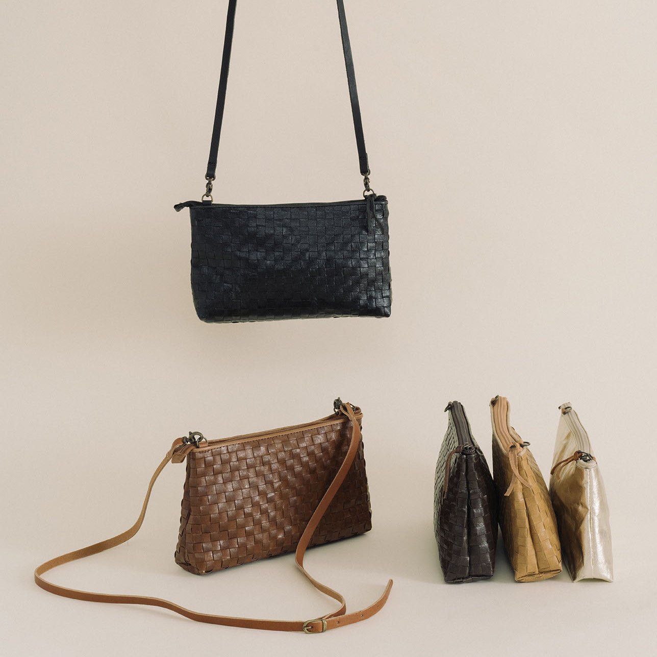 Five woven washable paper handbags are shown, one hanging, four on a surface. They are black, brown, chocolate brown, tan and metallic.