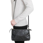 A woman is shown smiling in casual clothing, wearing a small washable paper handbag in woven black, with a long strap.