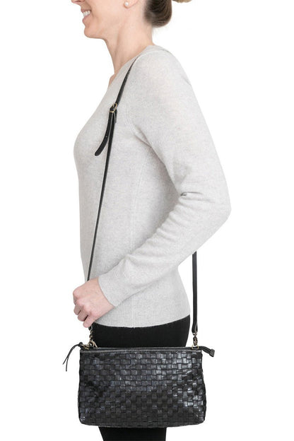 A woman is shown smiling in casual clothing, wearing a small washable paper handbag in woven black, with a long strap.