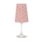 A pink washable paper lampshade with cut out details is shown sitting atop a wine glass.