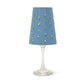 A blue washable paper lampshade with cut out details is shown sitting atop a wine glass. 