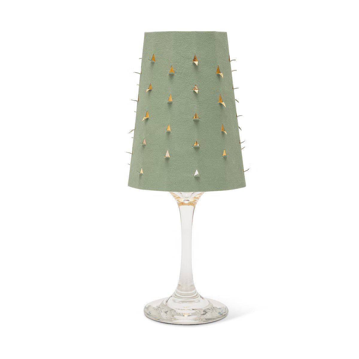 A sage green washable paper lampshade with cut out details is shown sitting atop a wine glass.