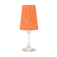 An orange washable paper lampshade with cut out details is shown sitting atop a wine glass.