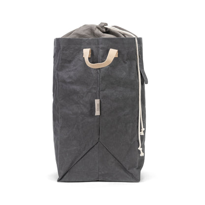 A washable paper laundry bag is shown in dark grey from a side angle. It features two side handles, a popper tab, and an interior drawstring lining.