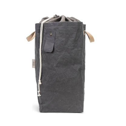A washable paper laundry bag is shown in dark grey. It features two side handles, a popper tab, and an interior drawstring lining.