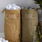 Two washable paper tall bags sit nestled together by popper closures, in a home setting. The one at left is tan and labelled "paper" and the one at right is khaki and labelled "plastic."