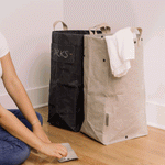 A GIF shows a woman labelling her washable paper laundry bags. The one at left is labelled "darks" and is black, and the one at right is grey and labelled "lights."